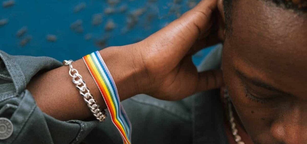 Crop pensive black man wearing rainbow bracelet and touching neck