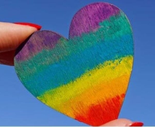 a close-up of a hand holding a rainbow-colored heart