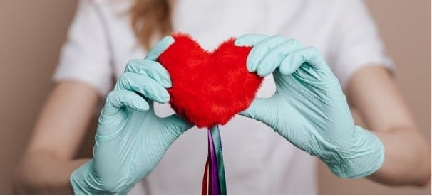 A doctor holding a heart with ribbons and thinking about affirming menstrual care for trans and nonbinary people 
