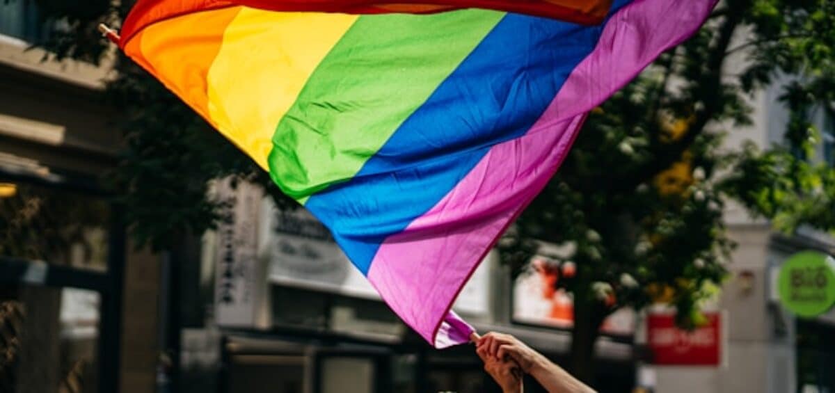 A person waving a rainbow-colored flag in the middle of a street.