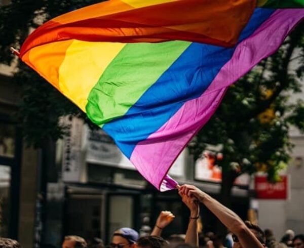 A person waving a rainbow-colored flag in the middle of a street.